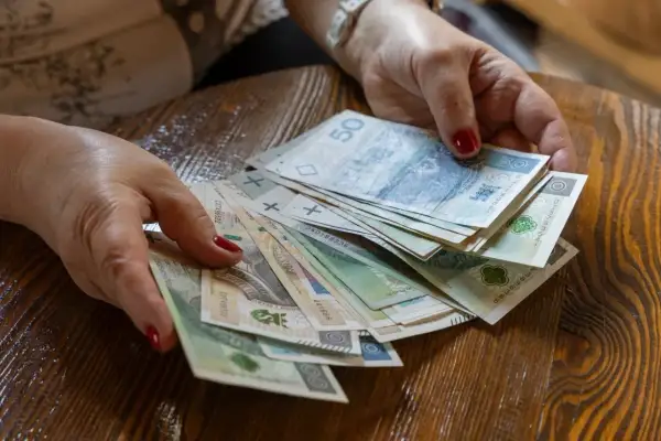 Dłonie trzymają stos polskich banknotów. Zastanawiasz się, ile wynosi podatek od darowizny 100 tys.?
