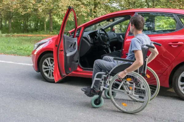 Uomo in carrozzina accanto a un'auto rossa, pronto per il passaggio di proprietà auto disabile decesso.