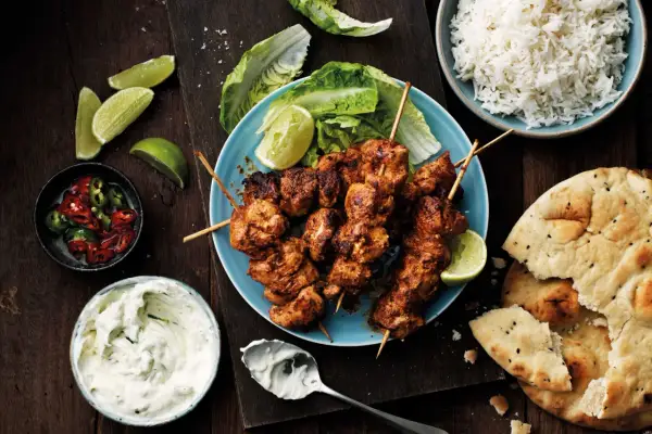 Tandoori kyckling på spett, serverad med ris, naanbröd, raita och limeklyftor.