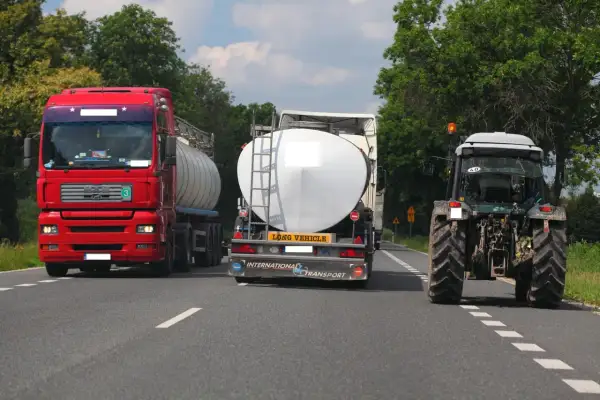 Czerwona ciężarówka próbuje wyprzedzanie na trzeciego, omijając traktor i inną cysternę na wąskiej drodze.
