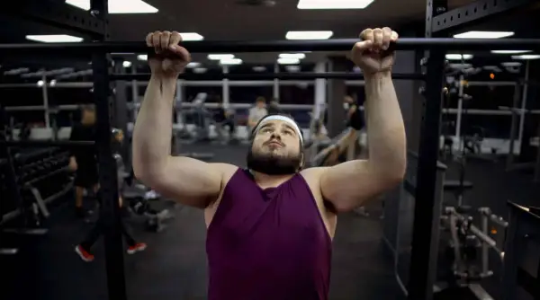 Uomo con fisico endomorfo si allena in palestra, concentrato su una trazione alla sbarra.