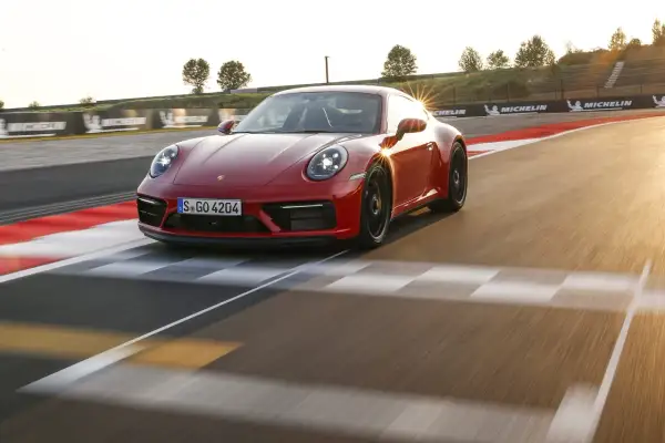 Czerwone Porsche 911 GTS sunie po torze wyścigowym, odbijając promienie zachodzącego słońca.