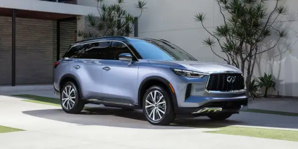 Elegancki, srebrny Infiniti QX60 parkuje przed nowoczesnym domem, otoczony bujną zielenią.