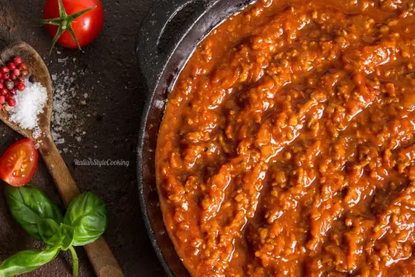 Herzhafte Bolognese-Sauce in einer Pfanne, mit frischen Tomaten, Basilikum, Salz und Pfefferkörnern als Zutaten für Bolognese.