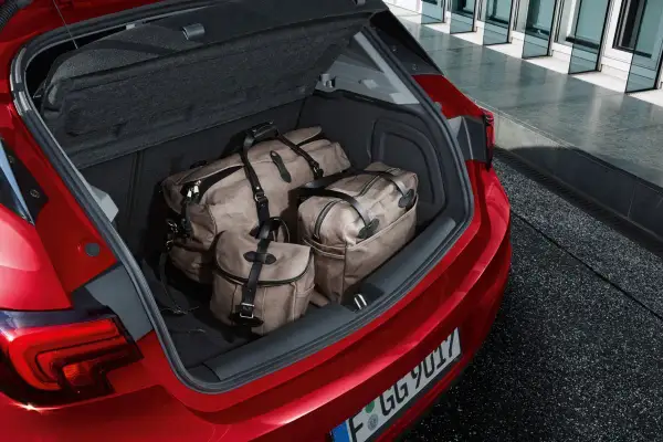 Bagażnik czerwonego Opla Astry J hatchback wypełniony trzema stylowymi torbami podróżnymi.