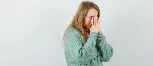 Een vrouw met blond haar, die haar gezicht bedekt met haar handen, lijkt overprikkeld, wat kan duiden op hsp en trauma.