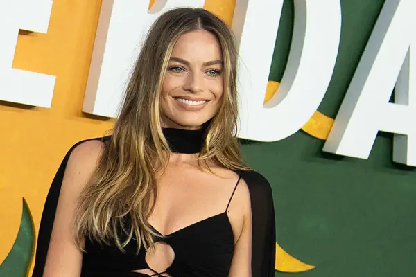 Margot Robbie sonríe con un vestido negro. La pregunta de cuanto mide Margot Robbie es un misterio, pero su estilo es innegable.