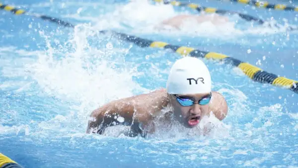 A swimmer in a white cap and goggles powers through the water, demonstrating technique for how to swim faster.