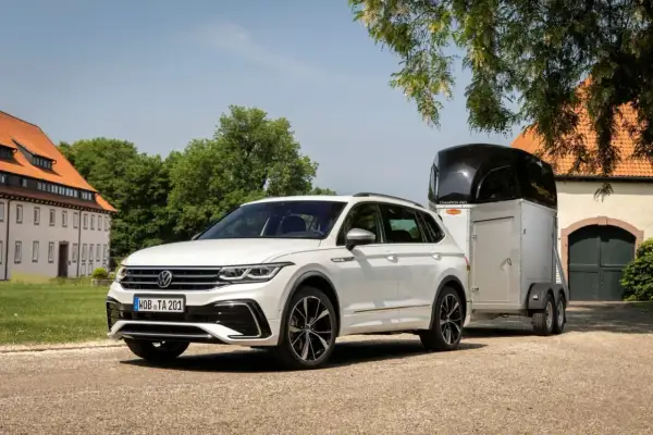 Biały Volkswagen SUV z przyczepą do przewozu koni stoi przed starym budynkiem.