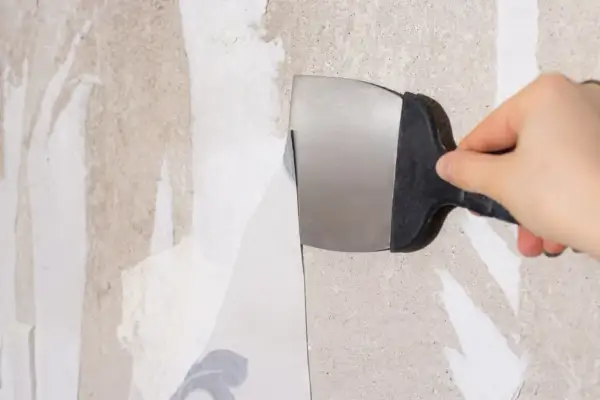 Maintenant, il faut enlever la moquette collée sur béton. Une spatule métallique décolle le revêtement mural.