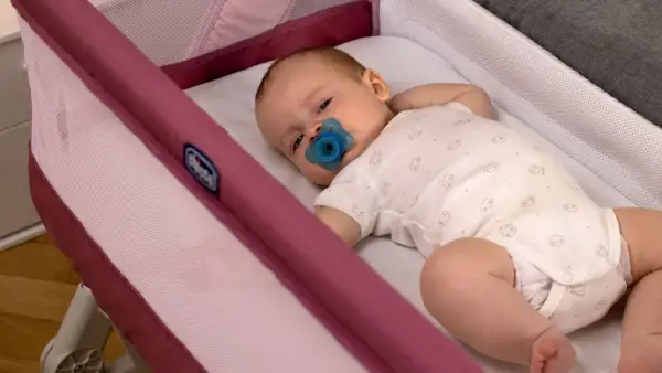 Un neonato con ciuccio dorme sereno nella sua culla, un luogo sicuro dove far dormire un neonato.