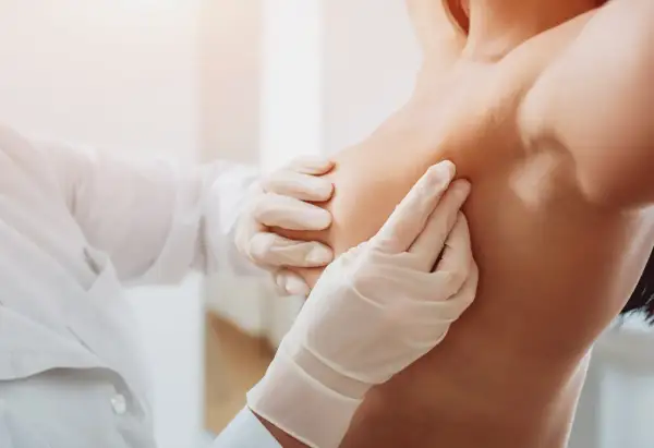 Lekarz w białej rękawiczce delikatnie bada pierś, lokalizując znacznik tytanowy po biopsji.