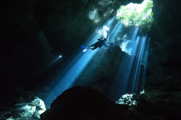 Buceadores exploran la asombrosa profundidad de un cenote, con rayos de luz solar atravesando la oscuridad.