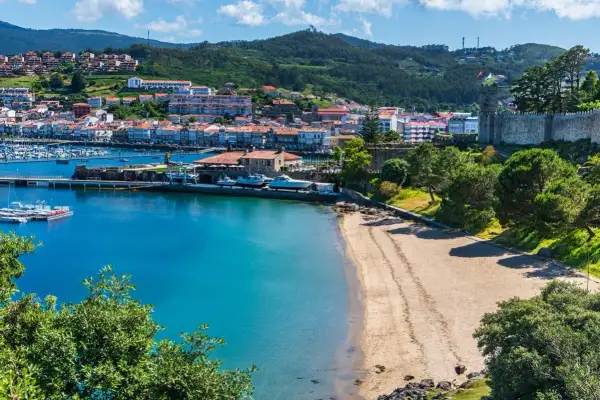 Bahía con barcos y un pueblo costero al fondo. Ideal para planificar como viajar barato por España y disfrutar de sus costas.