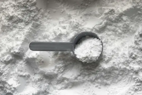 Miarka z białym proszkiem, prawdopodobnie tetrasodium glutamate diacetate, na tle sypkiego materiału.
