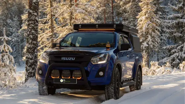 Niebieski Isuzu w zimowym lesie, z dodatkowymi światłami LED na dachu i zderzaku. Dowiedz się, jak ustawić żarówki LED w samochodzie, by podróżować bezpiecznie.