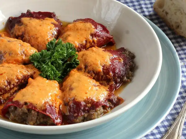 Pimientos rellenos de carne cubiertos con una cremosa salsa naranja, adornados con perejil fresco.