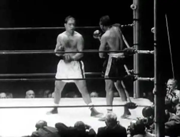 Two boxers in a ring. One boxer, possibly Rocky Marciano, is in the foreground, his reach evident as he prepares to strike.