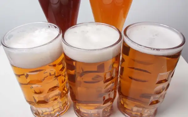 Tre bicchieri di birra dorata con schiuma bianca, uno più scuro e uno arancione sullo sfondo. Un invito a scoprire la differenza tra pils e lager.