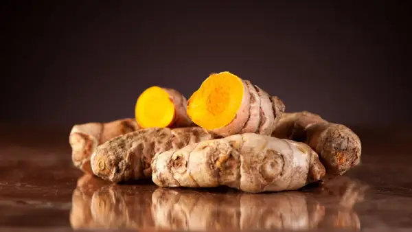 Ein Haufen frischer Kurkumawurzeln, eine davon aufgeschnitten, enthüllt ihr leuchtend orangefarbenes Inneres und die wertvollen Kurkuma Inhaltsstoffe.