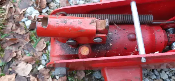 Detaljbild av en röd domkraft. En metallpinne sticker upp och en fjäder är synlig. Det ser ut som att det är dags att fylla olja i domkraften för att den ska fungera som den ska.