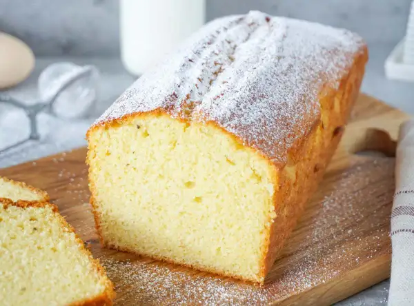 Ein saftiger Rührkuchen, bestäubt mit Puderzucker, ideal für einfache Kuchen Rezepte. Daneben liegen zwei Scheiben.