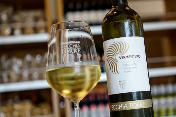 Un bicchiere di vino bianco, il vermentino è frizzante, accanto alla bottiglia Vecchia Torre.