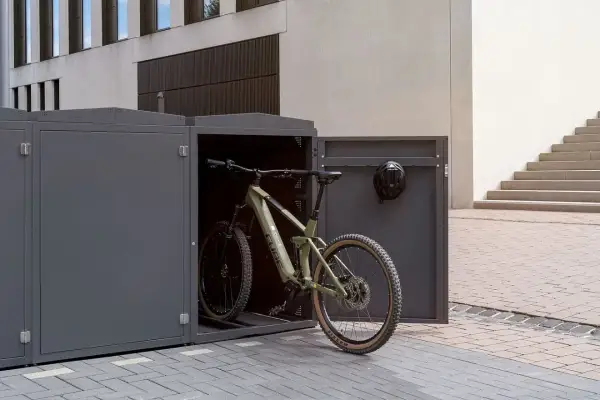 Ein grünes Mountainbike steht in einem modernen, grauen Fahrrad-Stellplatz. Ein Helm hängt an der Tür.