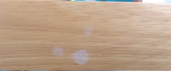 Trois petites taches blanches sur une surface en bois clair, comme des traces laissées par des gouttes d'eau séchées.
