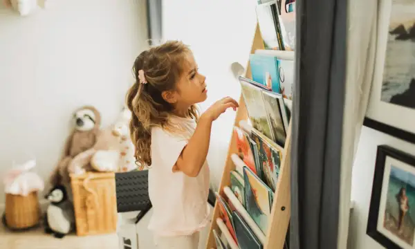 Een meisje met blond haar kijkt aandachtig naar de boekenplank, klaar om een nieuw avontuur te ontdekken. Ze houdt van lezen, kinderen.