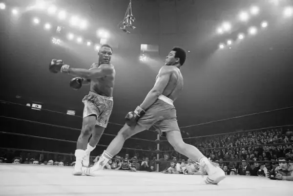 Two boxers clash in a dramatic moment. One out boxer throws a punch while the other dodges, the crowd watching intently.