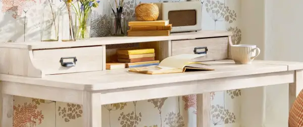 Scrivania chiara con cassetti, libri, tazza e radio vintage. Ideale per chi vuole imparare come verniciare un mobile da marrone a bianco.