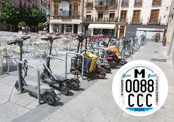 Patinetes eléctricos y bicicletas aparcados en una plaza. Se ve una pegatina de la DGT con la matricula CD.