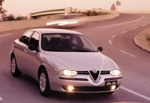En silverfärgad Alfa Romeo 156 kör på en kurvig väg i solnedgången.