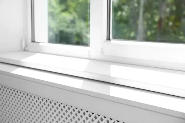 Biały parapet na równo ze ścianą, z widocznym kratkowanym grzejnikiem pod oknem.