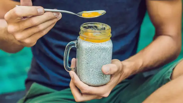 Mann hält ein Glas Chia-Pudding mit Mango-Topping. Die Frage "wieviel chiasamen pro tag" wird durch die gesunde Mahlzeit beantwortet.