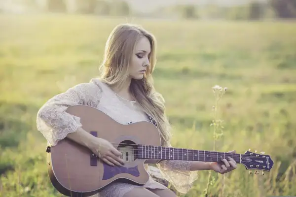 Dziewczyna gra na gitarze w plenerze. Czy wiesz, że gitara akustyczna ma swoje ciekawostki o muzyce?