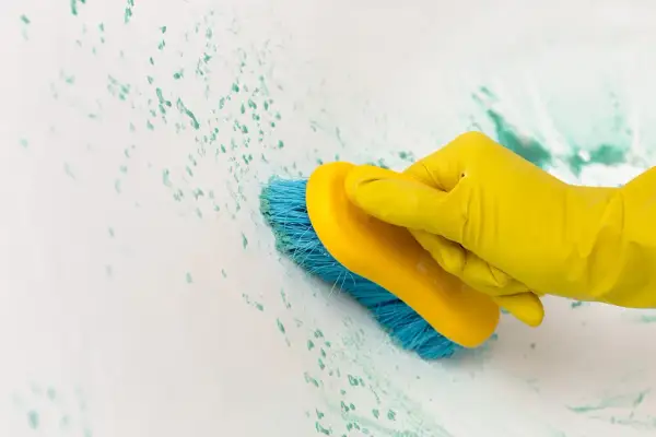 Main jaune, brosse bleue frottant une tache sur carrelage qui ne part pas.