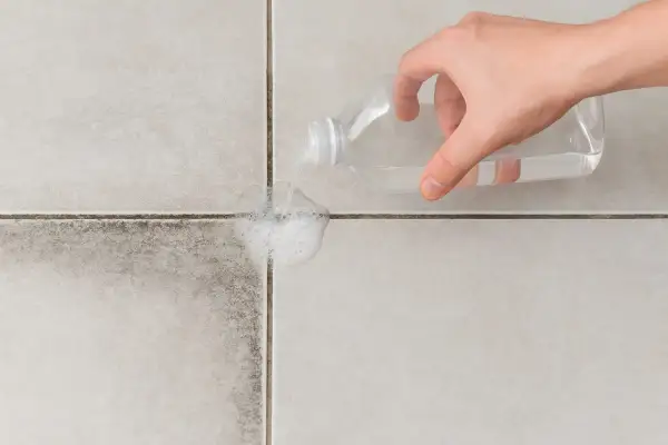Main d'une personne versant un produit nettoyant sur des joints de carrelage très encrassés pour les faire mousser.