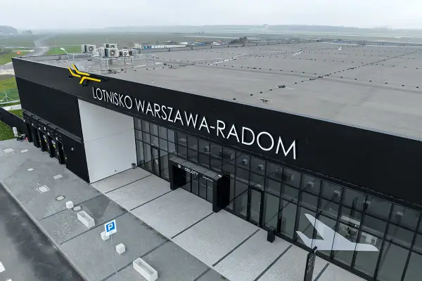Nowoczesny budynek lotniska Warszawa-Radom z napisem "ODLOTY" i symbolem samolotu na szkle.