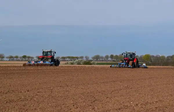 Deux tracteurs préparent le sol pour la culture du lin. Le champ est labouré, prêt pour les semis.