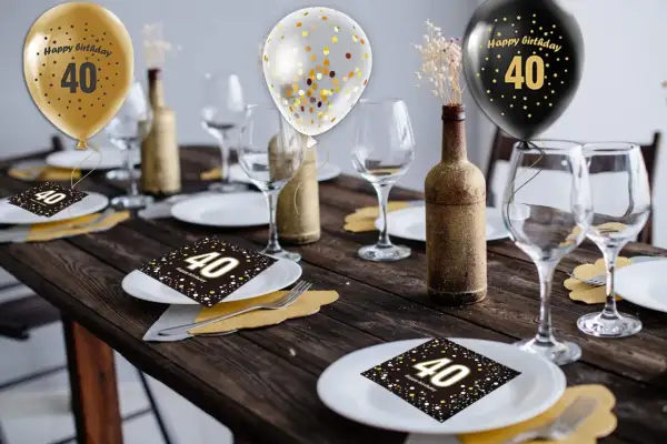 Elegancko udekorowany stół na 40 urodziny: złote i czarne balony, kieliszki, butelki i serwetki z cyfrą 40.