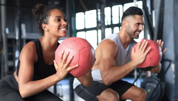 Coppia sorridente si allena in palestra con palle mediche. Non preoccuparti se il primo mese di palestra si ingrassa, è normale!