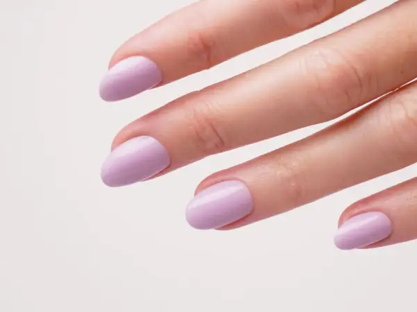 Une main aux ongles courts et arrondis, peints d'un joli violet pastel. Une idée ongle violet douce et élégante.