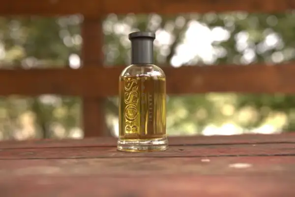 Szklana butelka perfum Boss Bottled Intense, z płynem o bursztynowym kolorze, stoi na drewnianym stole.
