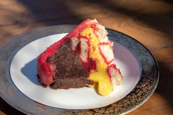 Una fetta di zuppa inglese, con pan di Spagna rosso e giallo e crema al cioccolato, su un piatto decorato.