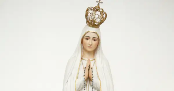 Figurka Matki Bożej Fatimskiej w białym welonie i złotej koronie, z rękami złożonymi do modlitwy.