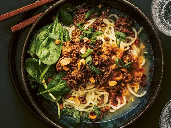 En skål med dan dan nudlar, toppad med köttfärs, jordnötter och sallad.