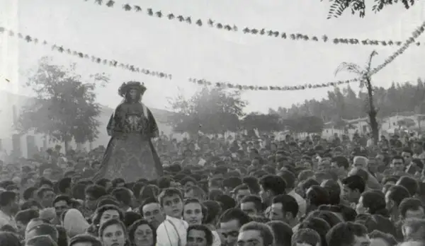 Una figura alta, vestida con traje tradicional, se alza sobre una multitud. Es parte de la **historia del Rocío**, una tradición ancestral.