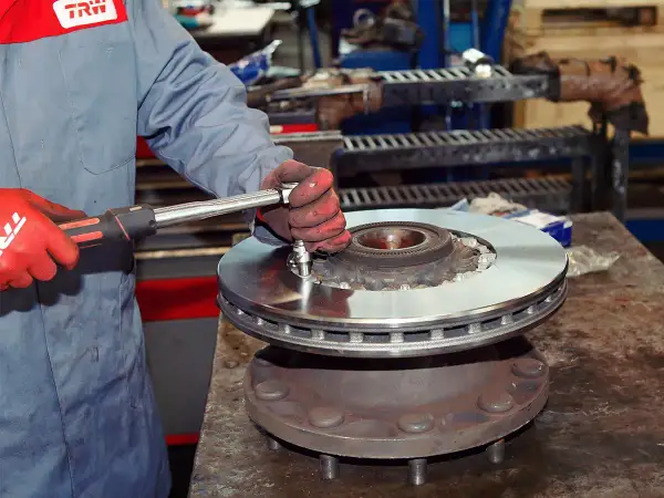 Mechanik w czerwonych rękawicach dokręca śruby podczas wymiany tarcz hamulcowych.
